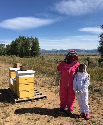 Katie Williams and her daughter Maggie in bee suits beside their hives near Pinedale